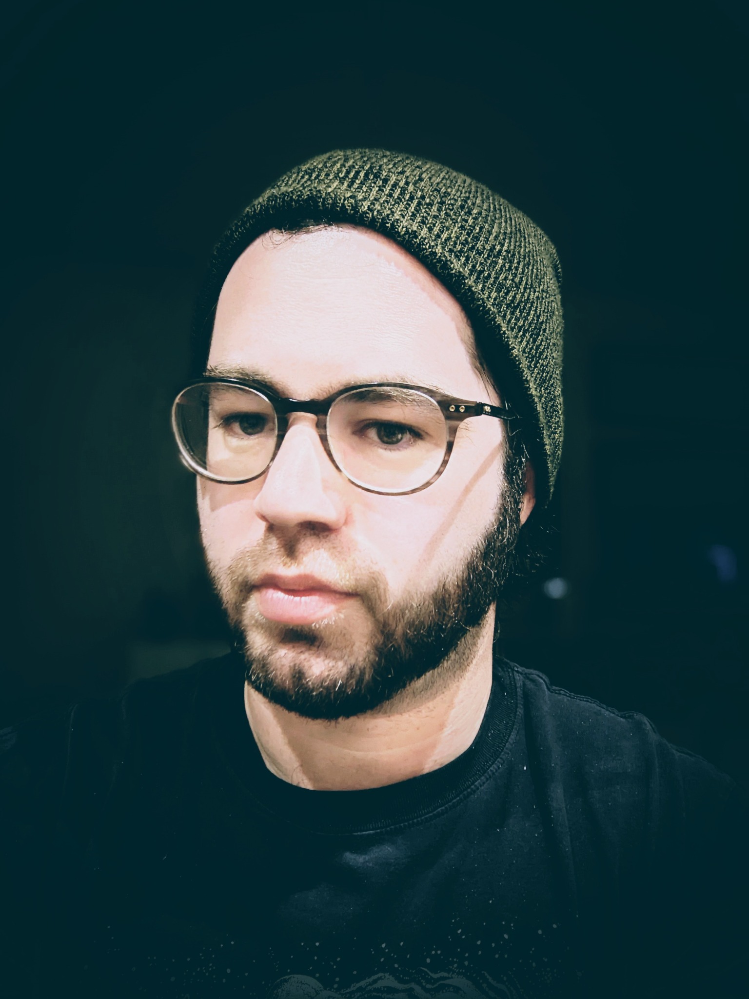 A portrait of a white man with glasses and a beard wearing a green knit cap